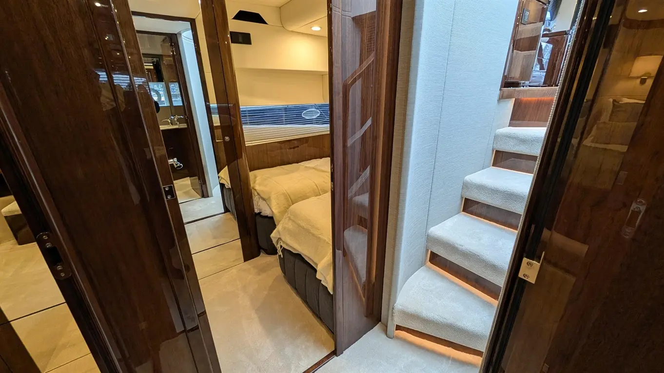 Spacious interior of a luxury yacht, featuring a sleeping area, staircase, and ensuite bathroom visible through doors.